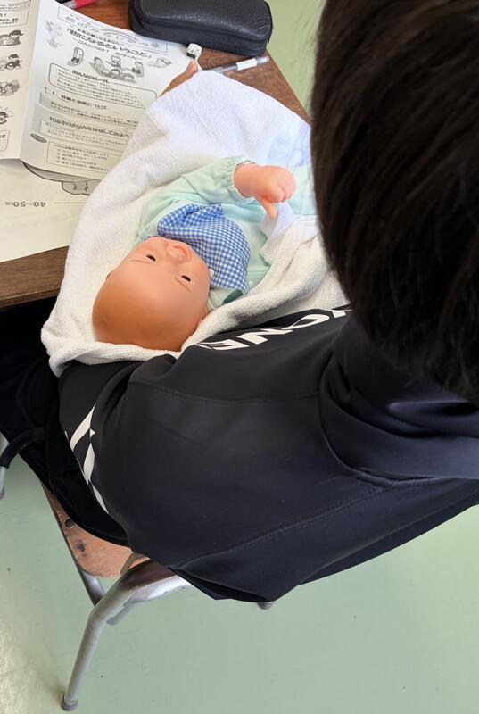 写真は、赤ちゃんの正しい抱き方を講師から学んでいる様子です。